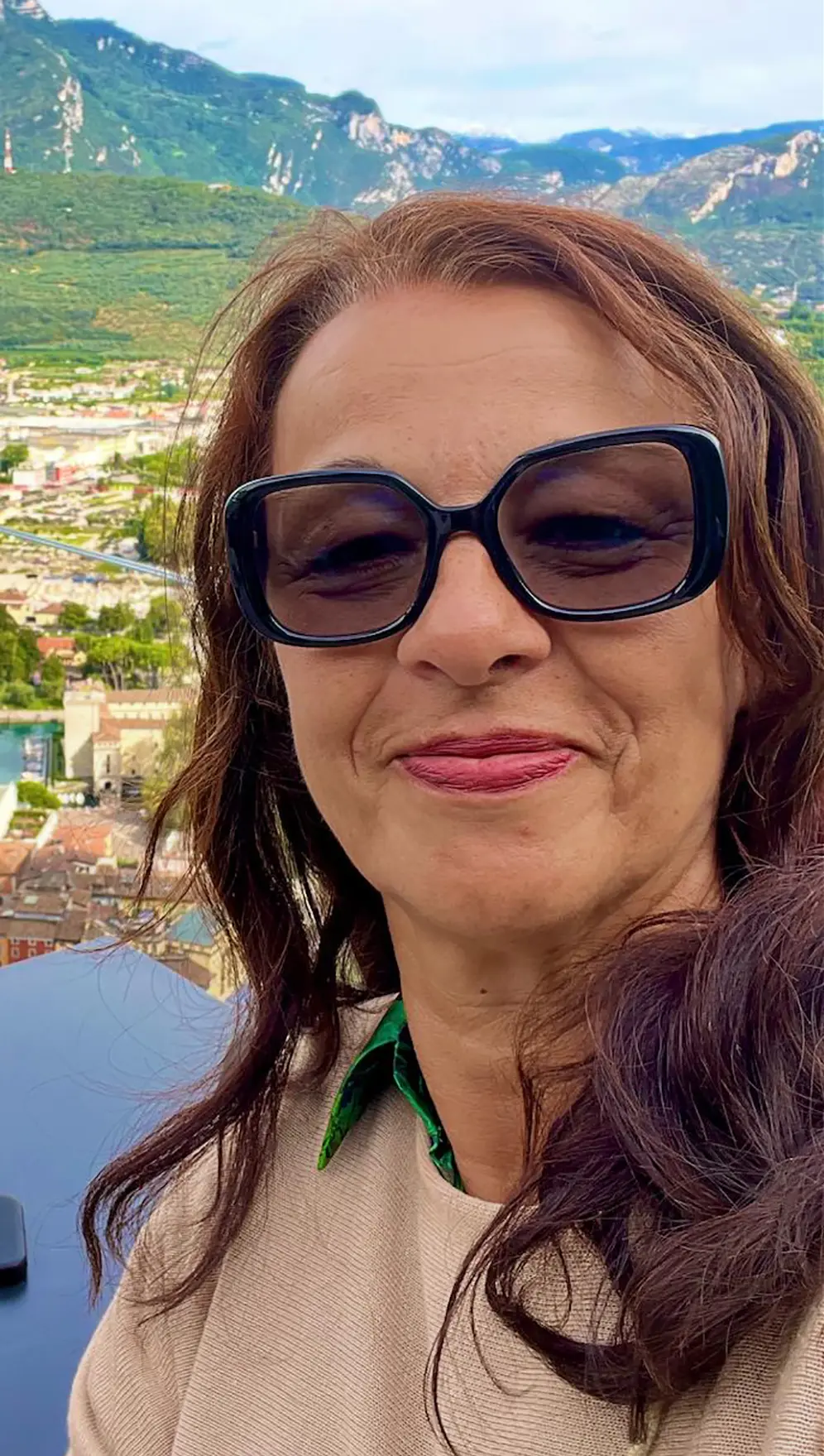 Porträt einer lächelnden Frau mit langen braunem Haar und schwarzer Sonnenbrille. 